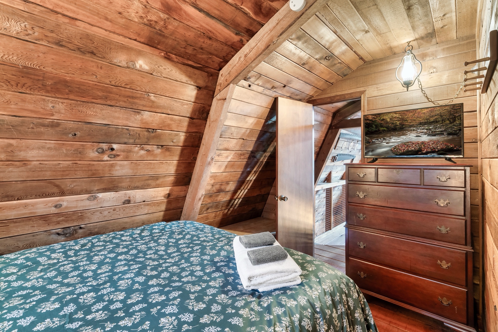 Second loft bedroom at Rustic Retreat with a dresser, mounted TV, and a pendant light by the doorway